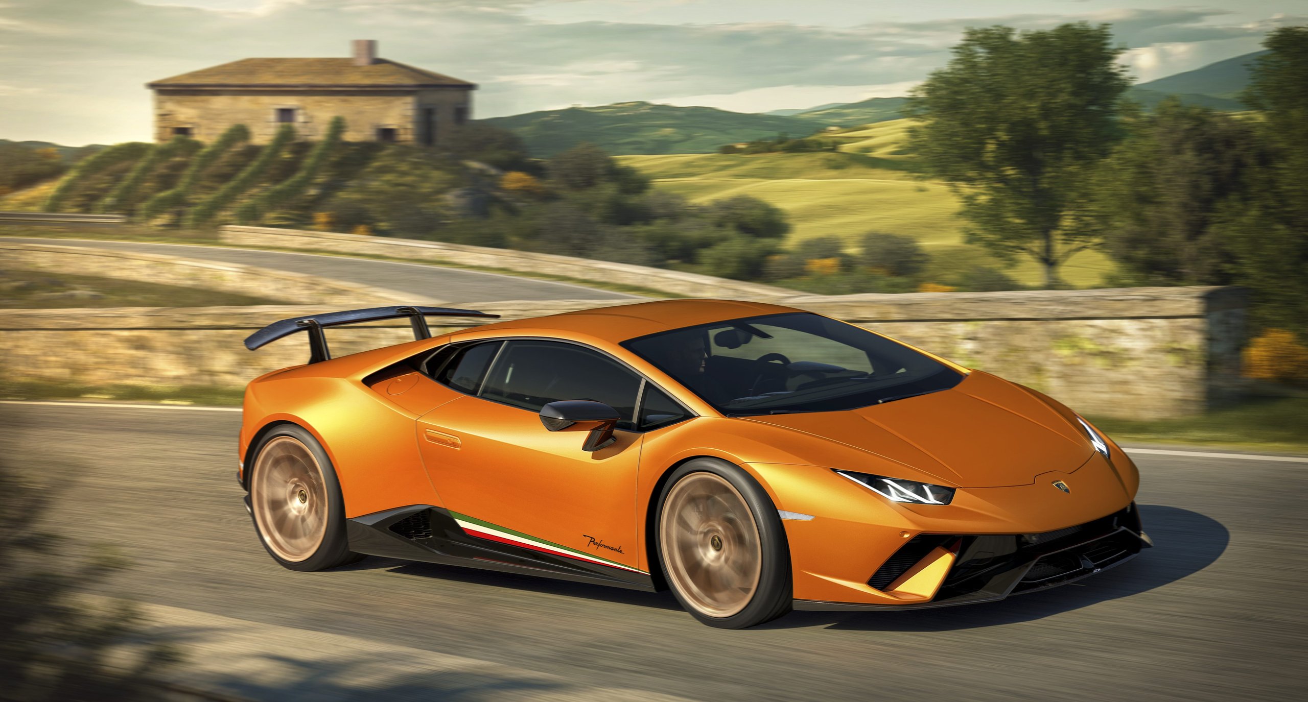 How The Huracán Performante Used Invisible Aerodynamics To Beat A 887-Hp Hybrid Around The Nürburgring 13 Orange huracán performante driving through italian countryside with traditional buildings and rolling hills in the background