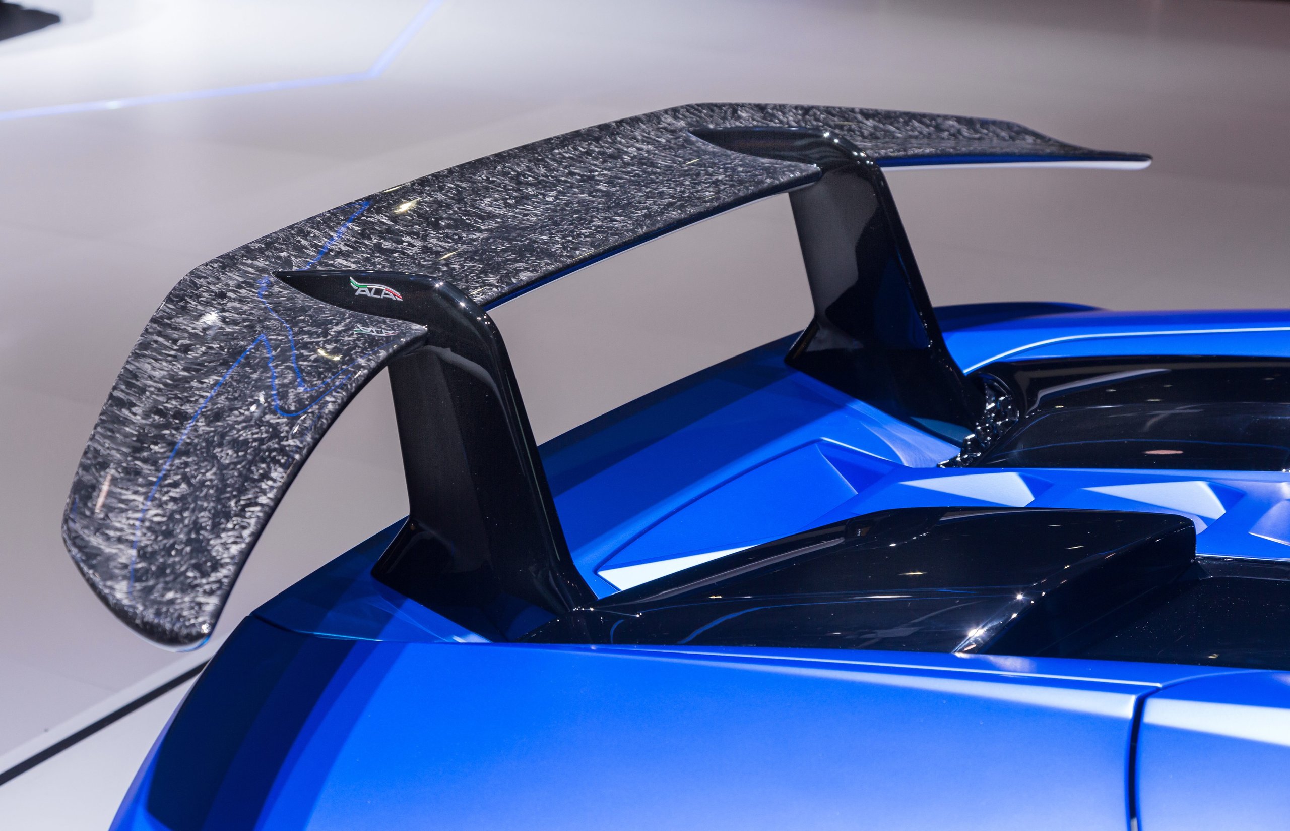 How Lamborghini Kept The Performante Spyder From Being A Compromise 5 Close-up of forged carbon fiber texture on the rear wing of a blue huracán performante spyder with italian flag detail