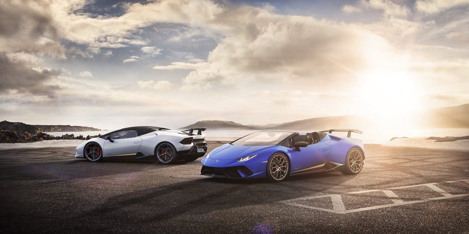 Blue Lamborghini Huracán Performante Spyder and white Performante coupe parked together at sunset by water