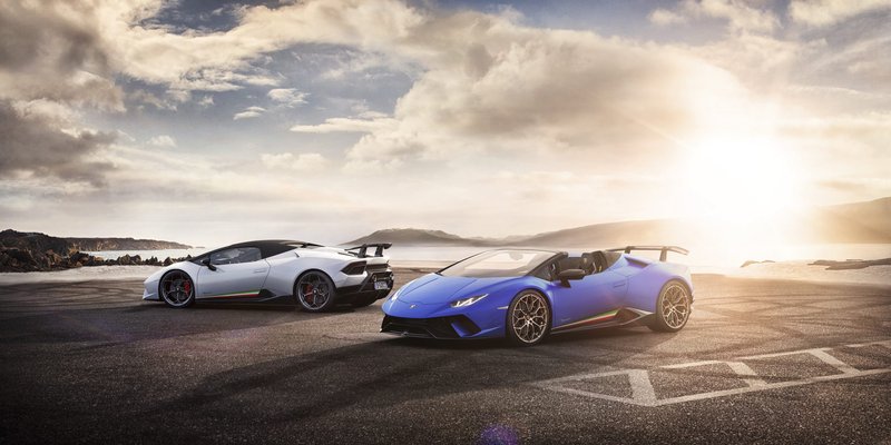 Blue Lamborghini Huracán Performante Spyder and white Performante coupe parked together at sunset by water