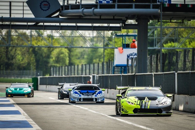 A line of Lamborghini Huracán Super Trofeo race cars on track at Monza, led by a yellow and black liveried car with aggressive aerodynamics and a prominent rear wing