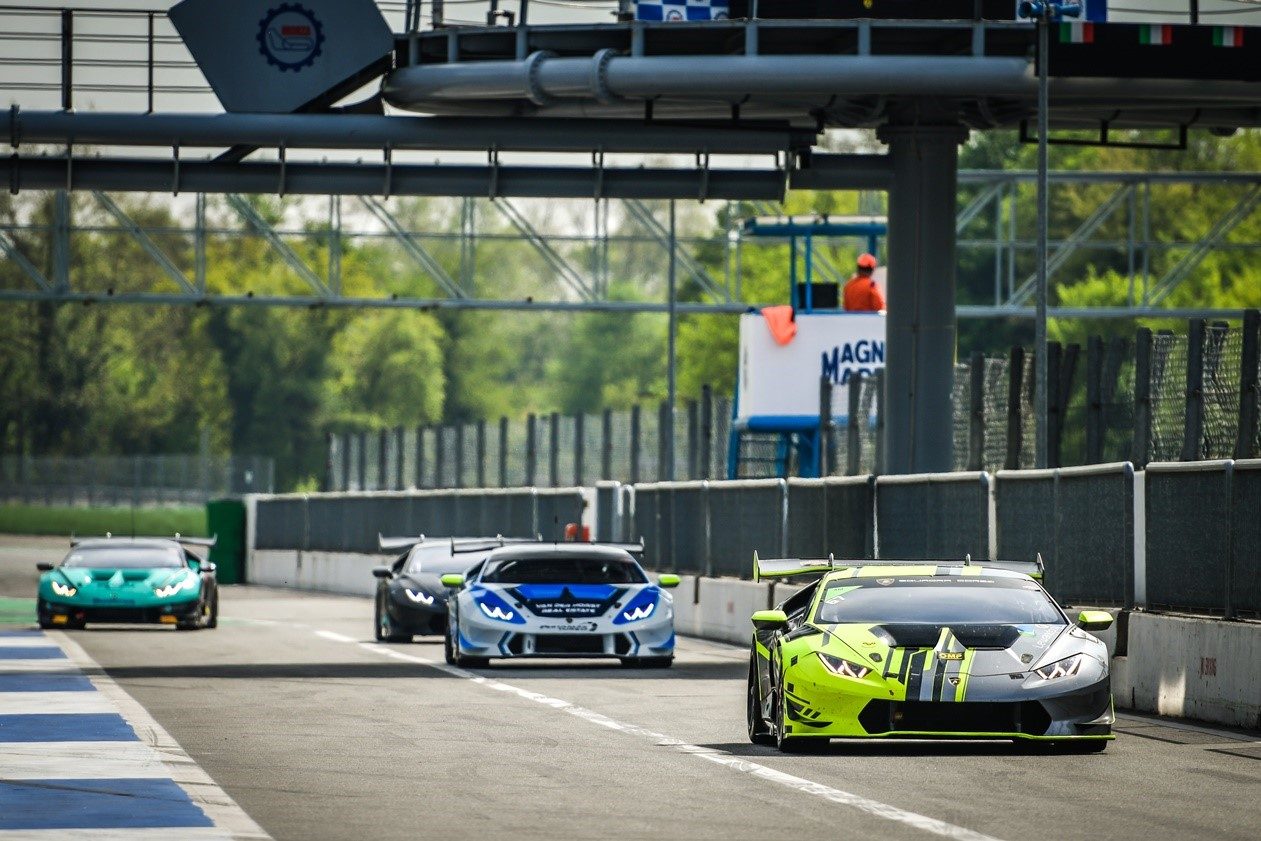 A line of Lamborghini Huracán Super Trofeo race cars on track at Monza, led by a yellow and black liveried car with aggressive aerodynamics and a prominent rear wing