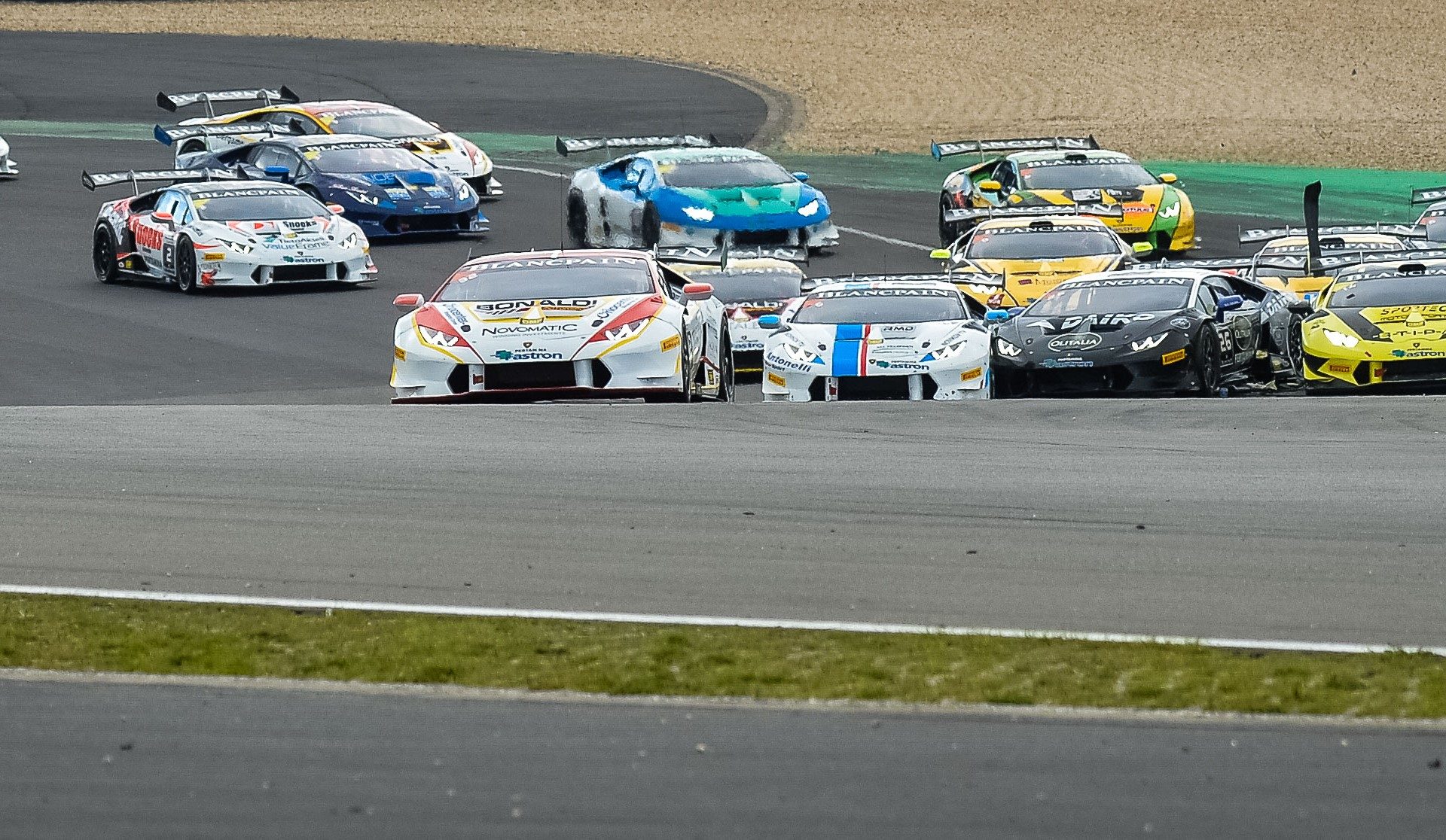 A pack of Lamborghini Huracan GT3 race cars in various liveries battling through a corner on a racetrack