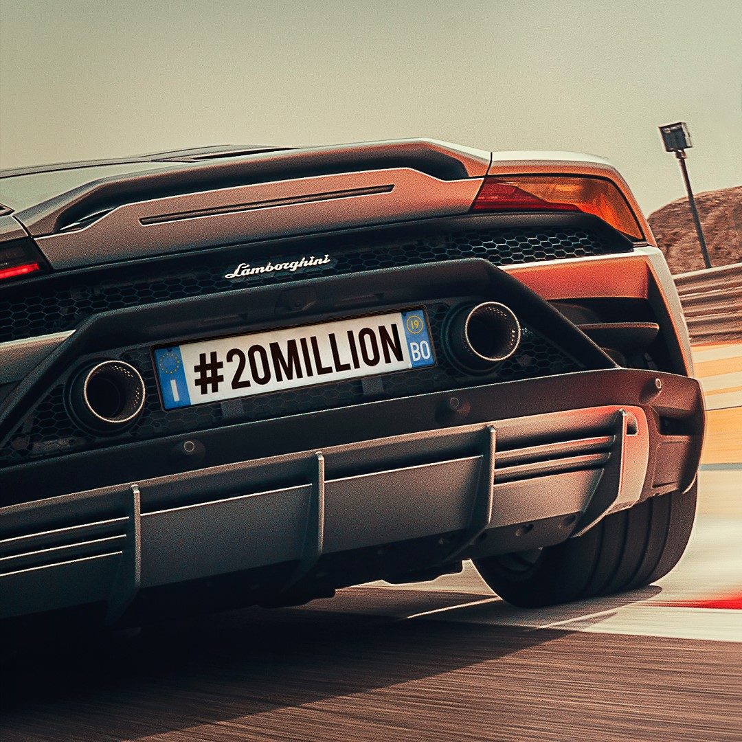 Rear three-quarter view of a matte grey Lamborghini Huracán on a racetrack with a custom license plate reading #20MILLION