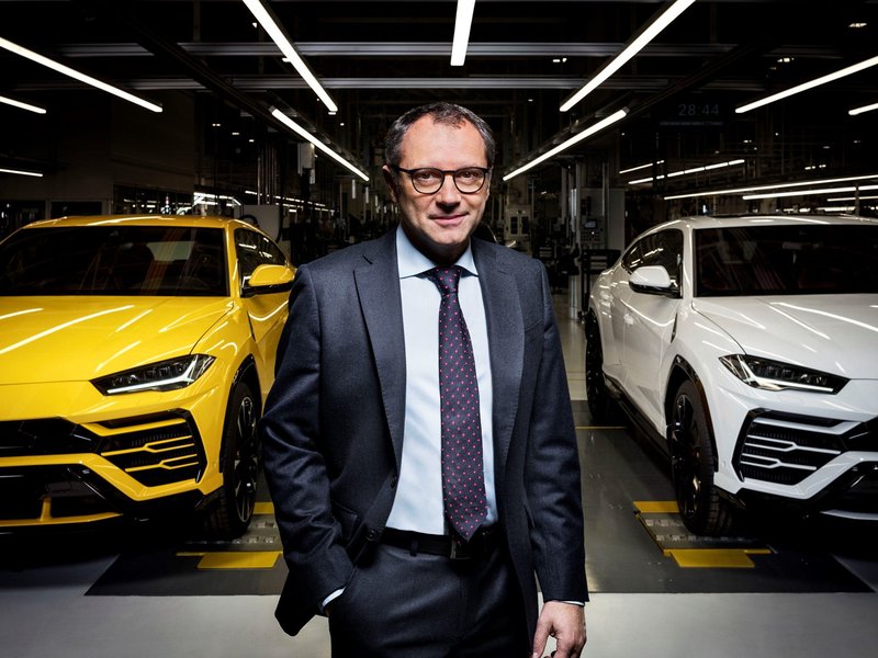 Lamborghini executive standing between a yellow and white Urus on the expanded Sant'Agata Bolognese factory floor