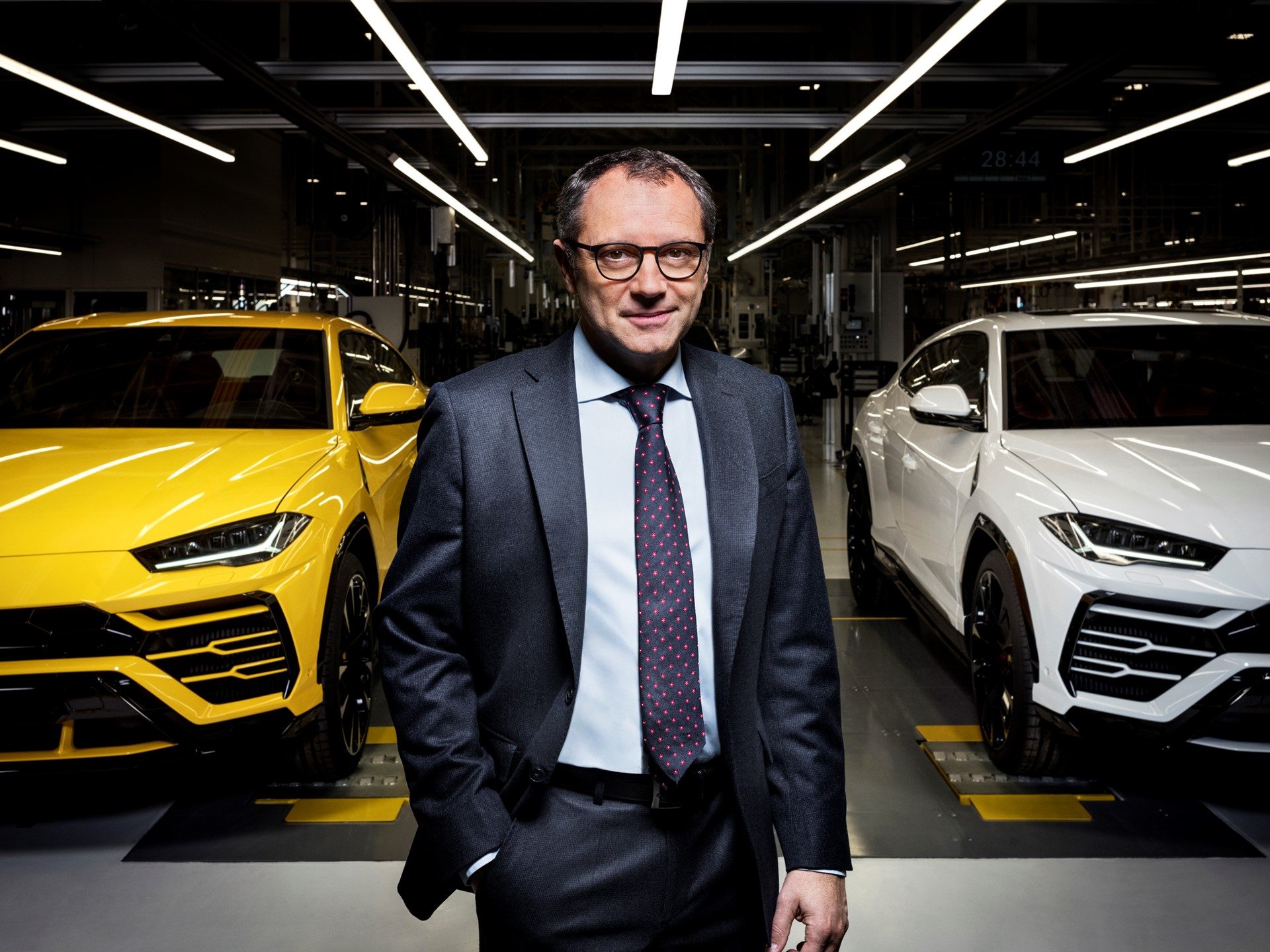 Stefano Domenicali stands between a yellow and white Lamborghini Urus on the Sant'Agata Bolognese factory floor