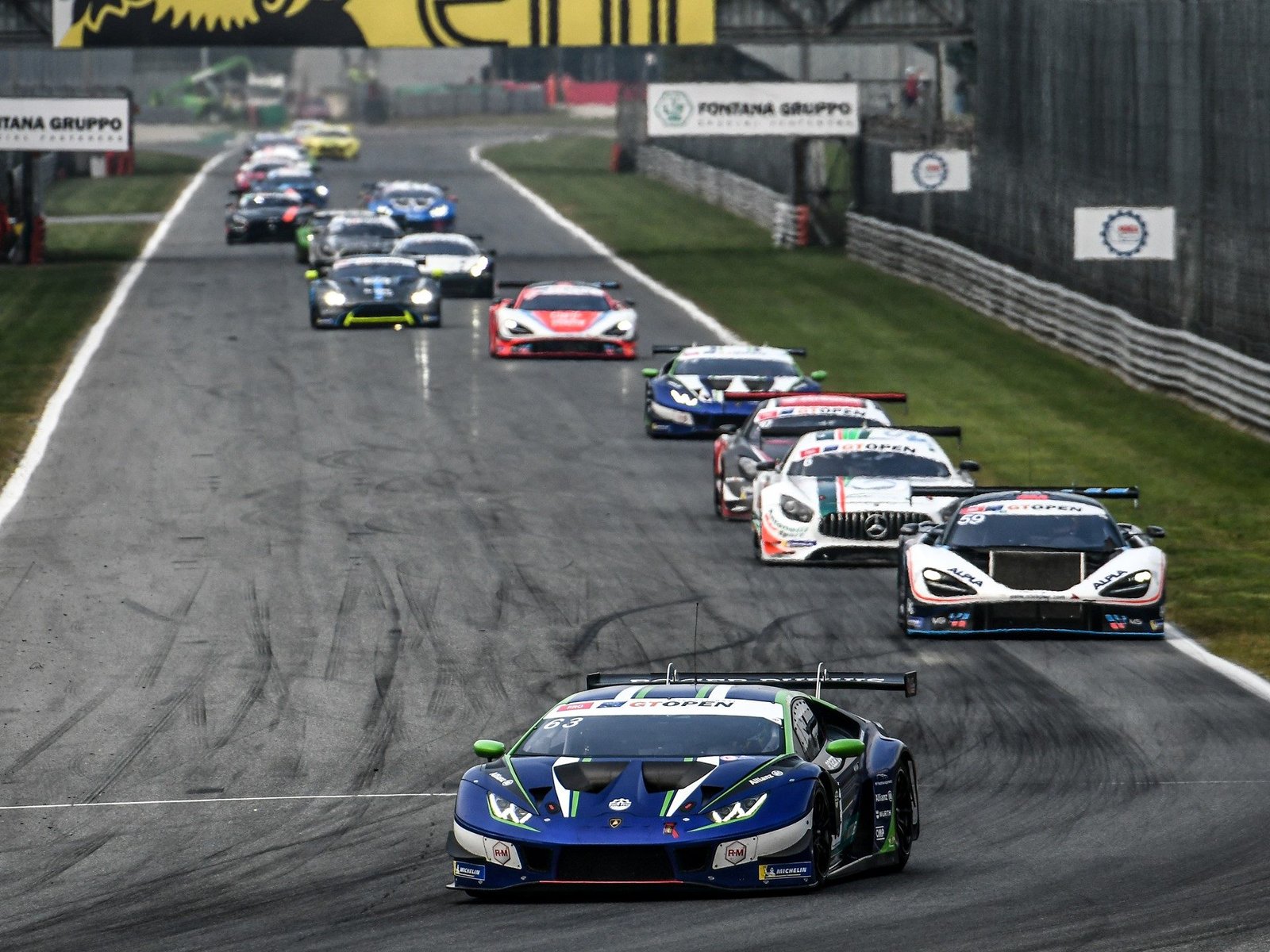 Lamborghini Huracán GT3 Evo race car leading competitors on a wet track, showing its aggressive aero kit and large rear wing