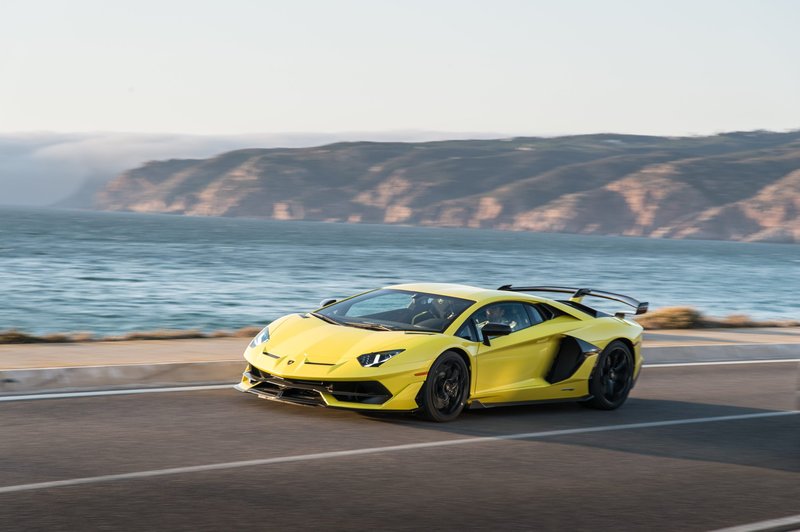 Yellow Lamborghini Aventador SVJ driving on a coastal road with ocean and cliffs in the background