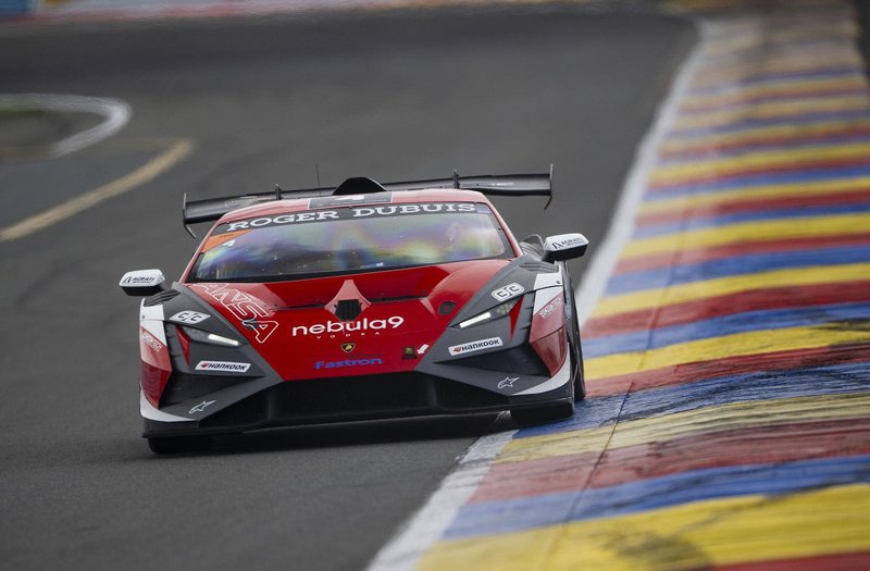 A red and black Lamborghini Huracán GT3 EVO2 race car navigating a wet corner on a racetrack