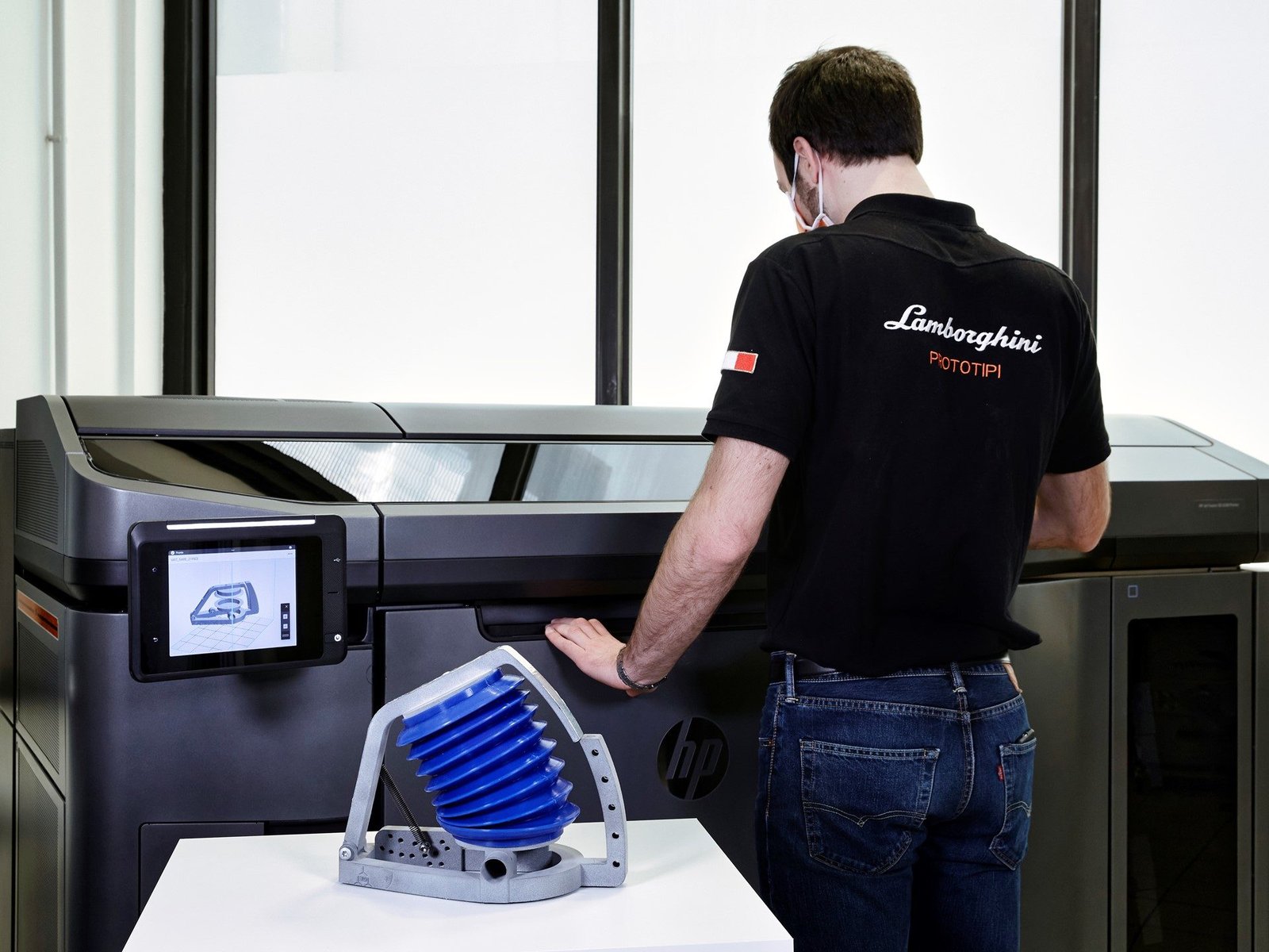 Lamborghini PROTOTIPI employee operating HP Jet Fusion 3D printer with 3D-printed breathing simulator component on table in foreground
