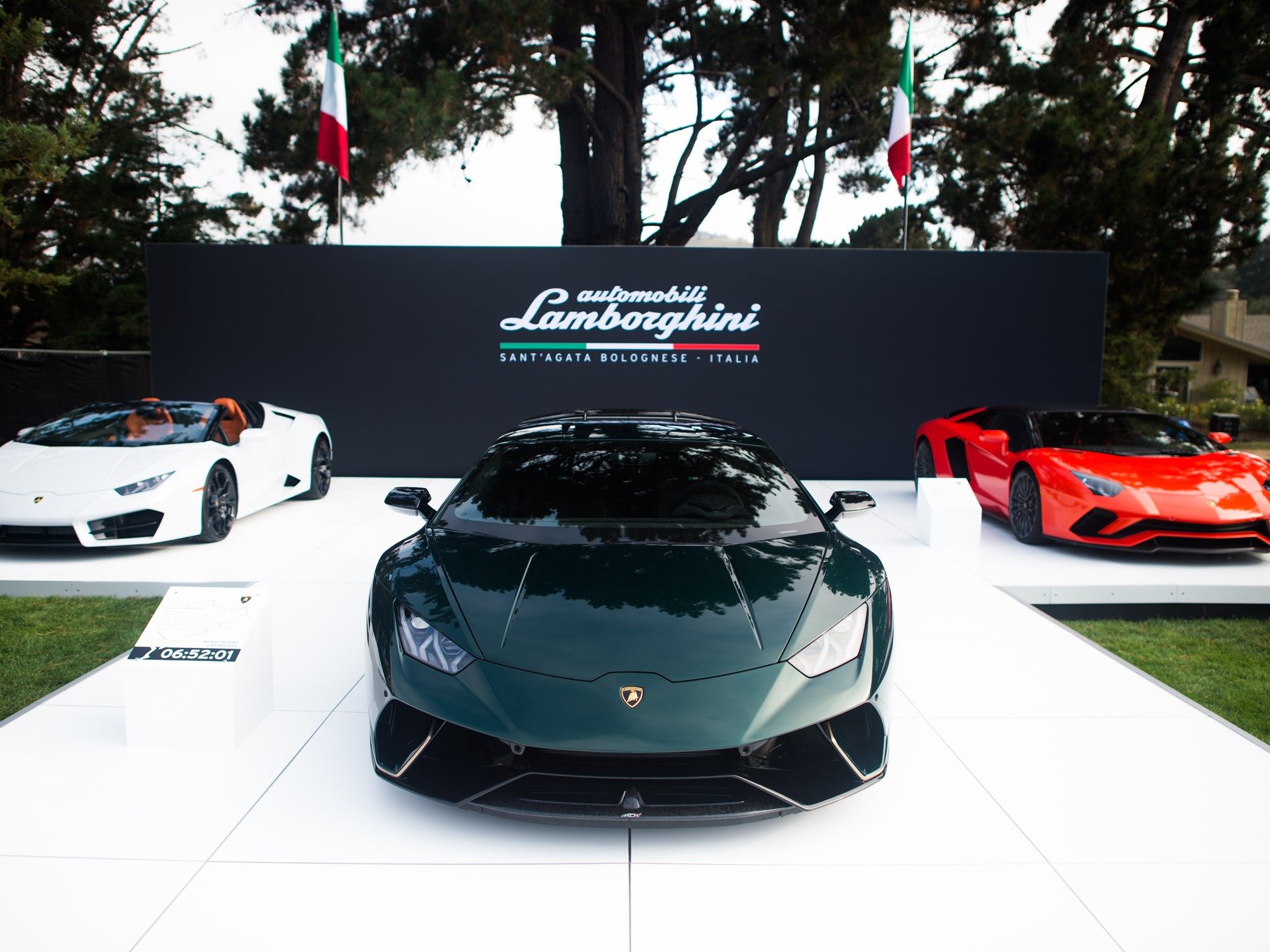 Three Lamborghini Ad Personam vehicles displayed on a white platform at Monterey Car Week 2017 with Italian flags and Lamborghini branding
