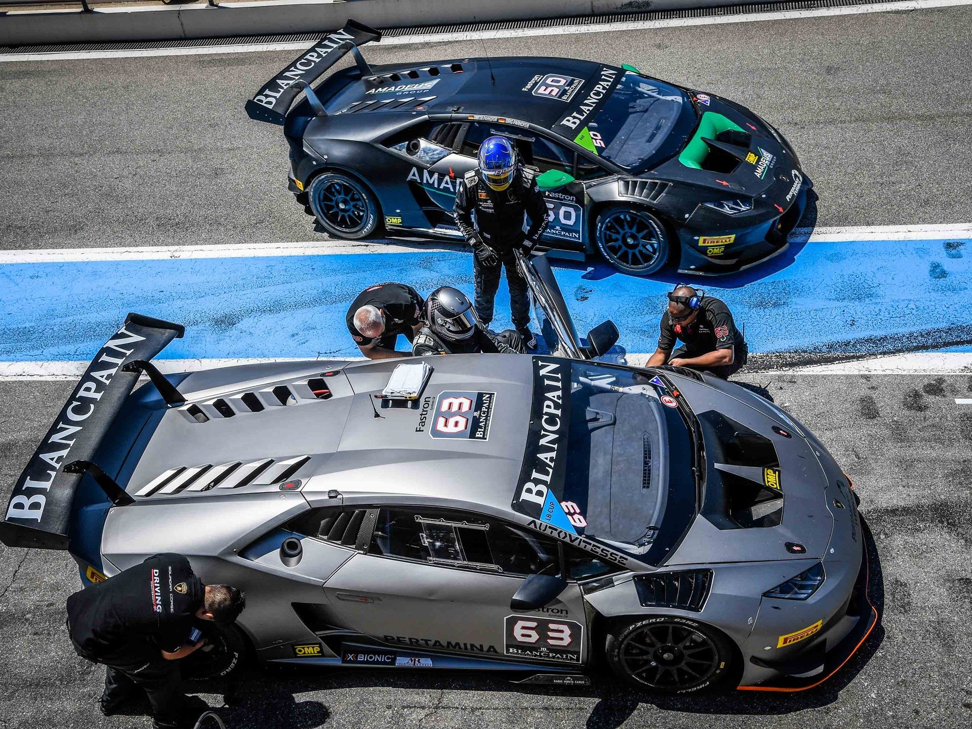 Two Lamborghini Huracán GT3 race cars in the pit lane with crew members attending to them during a Blancpain GT Series event