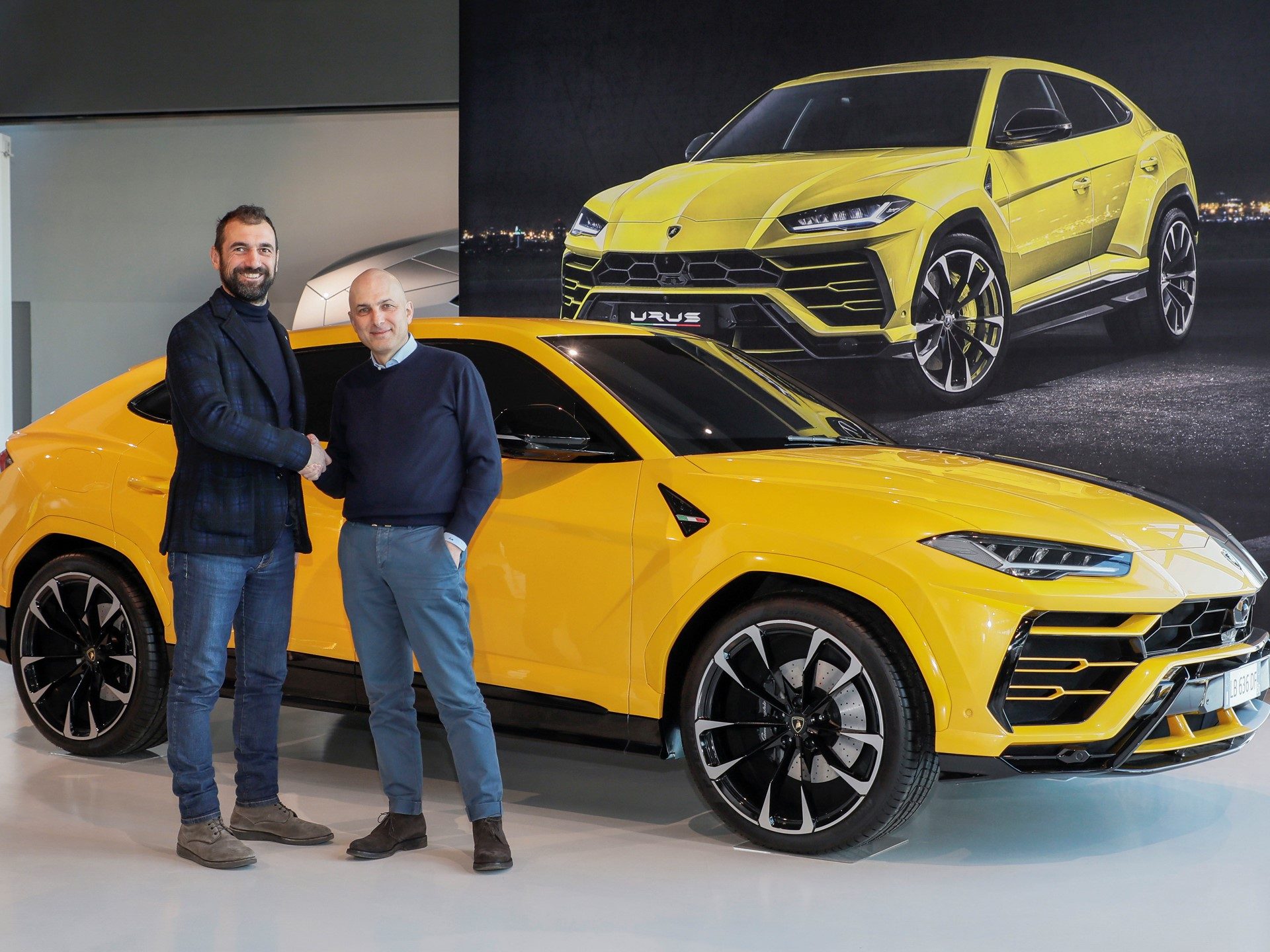 Executives shake hands in front of a yellow Lamborghini Urus to mark the Collezione Automobili Lamborghini and Bumper children's shoe collaboration