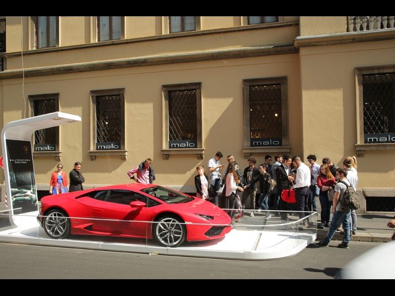 Red Lamborghini Huracán LP 610-4 displayed on a white platform at Audi City Lab, drawing a crowd of onlookers