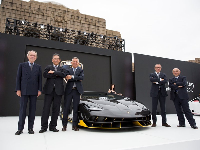Black Lamborghini Centenario Roadster with yellow accents displayed at the Excellence in Carbon Fiber event in Tokyo, with executives surrounding the car