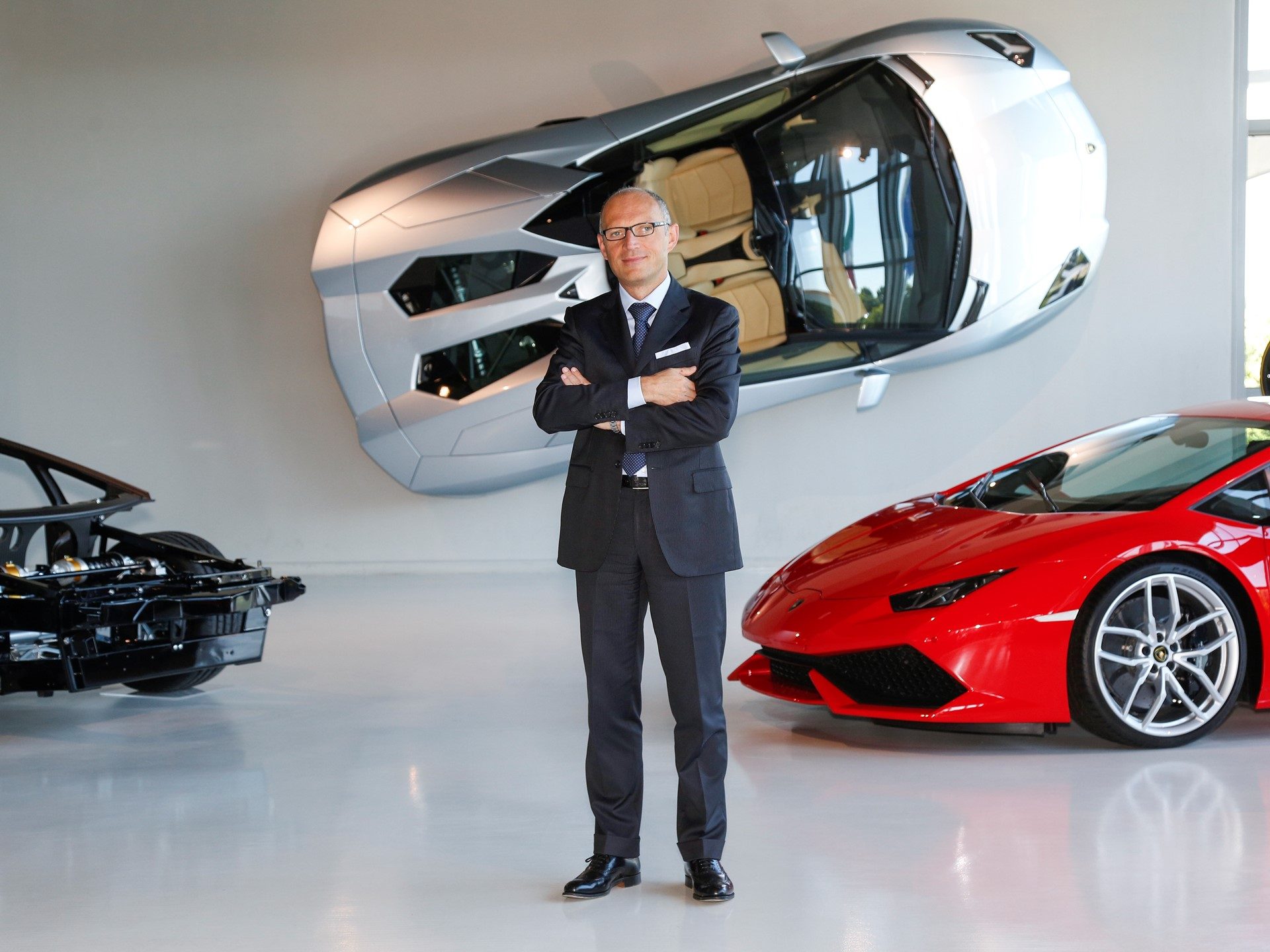 Paolo Poma standing in a Lamborghini showroom with a red Huracan and exposed Aventador chassis behind him