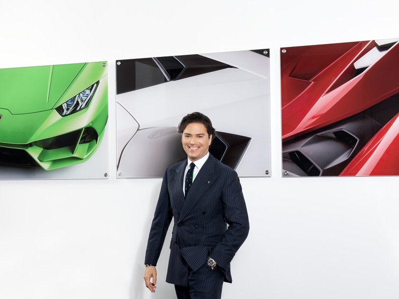 Giovanni Perosino standing in front of framed Lamborghini Huracan and Aventador images at Automobili Lamborghini headquarters
