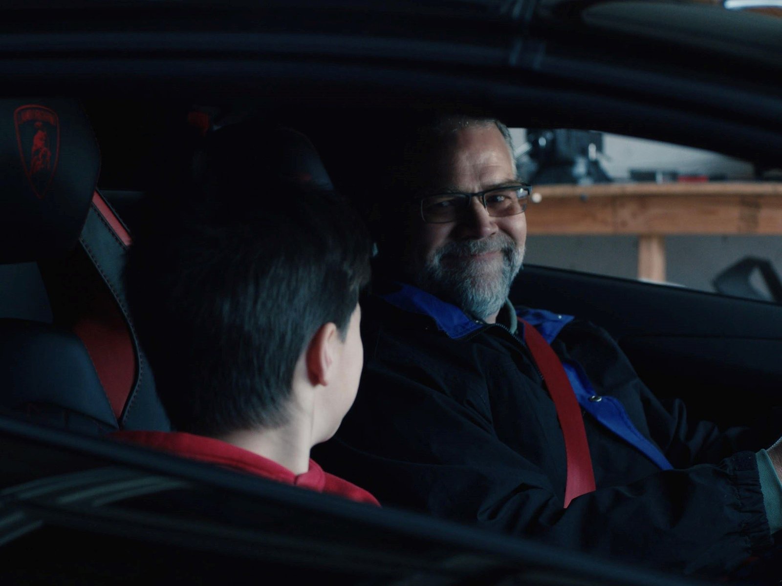 Sterling and Xander Backus seated inside the real Lamborghini Aventador S, with red leather stitching and the Lamborghini crest visible on the seatback