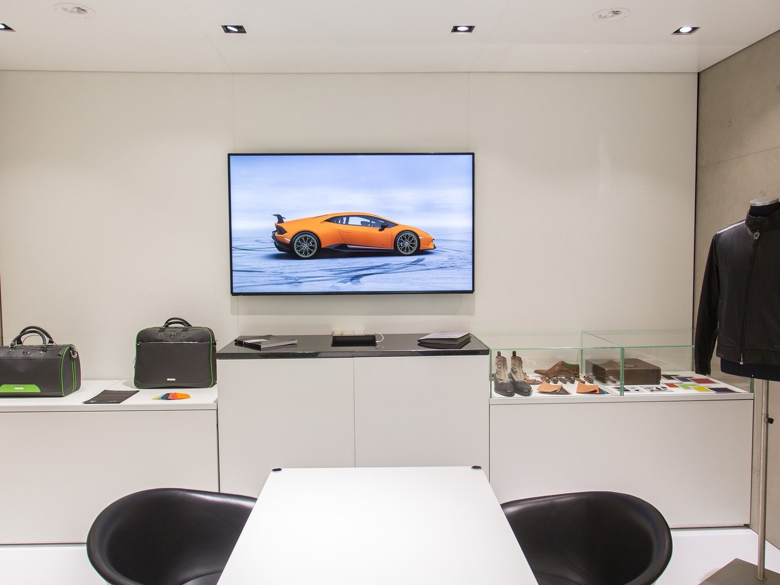 Lamborghini Collezione Automobili Lamborghini display with branded bags, shoes, color swatches, and a Huracan on the background screen
