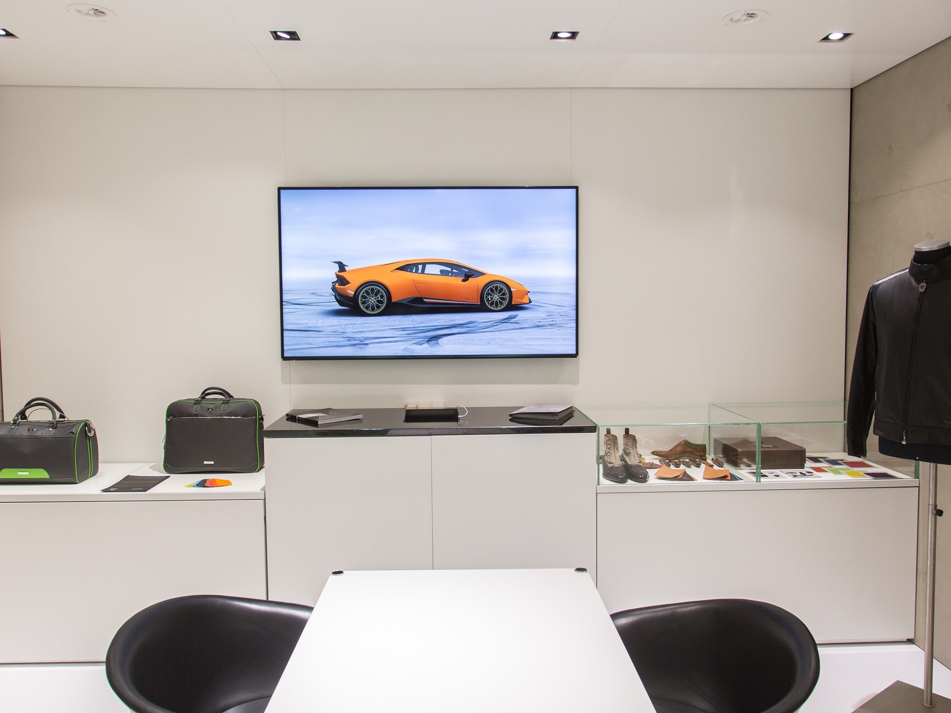 Lamborghini Collezione Automobili Lamborghini display with branded bags, shoes, color swatches, and a Huracan on the background screen