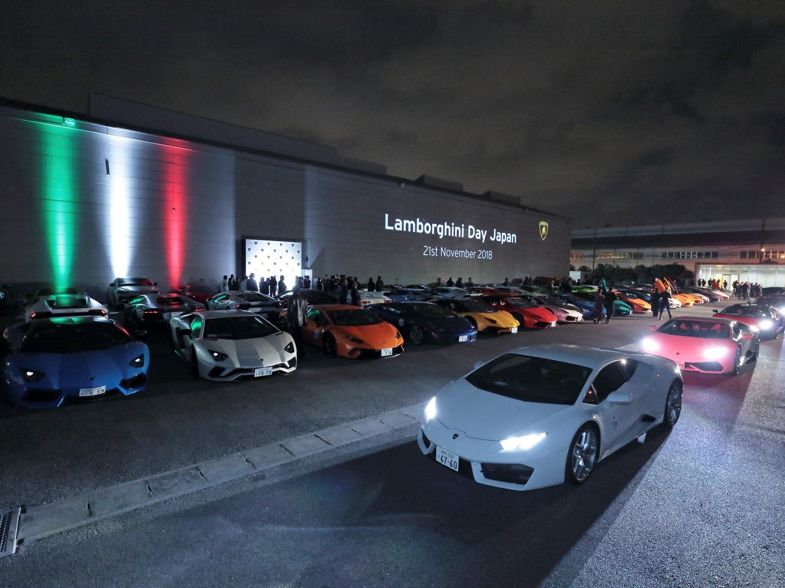 Over 200 Lamborghini models gathered at night during Lamborghini Day Japan 2018 in Yokohama, with Italian flag colors illuminating the venue building