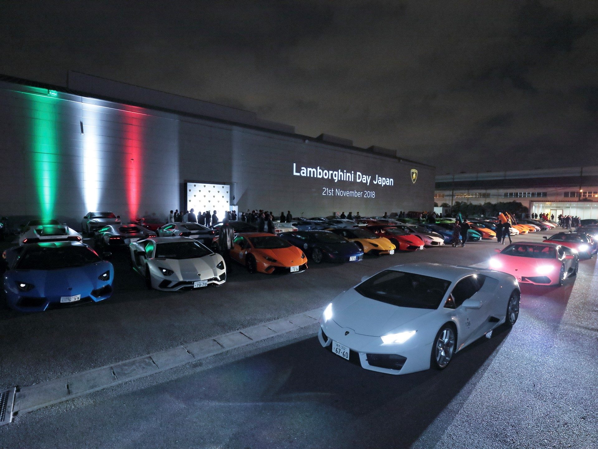 Over 200 Lamborghini models gathered at night during Lamborghini Day Japan 2018 in Yokohama, with Italian flag colors illuminating the venue building