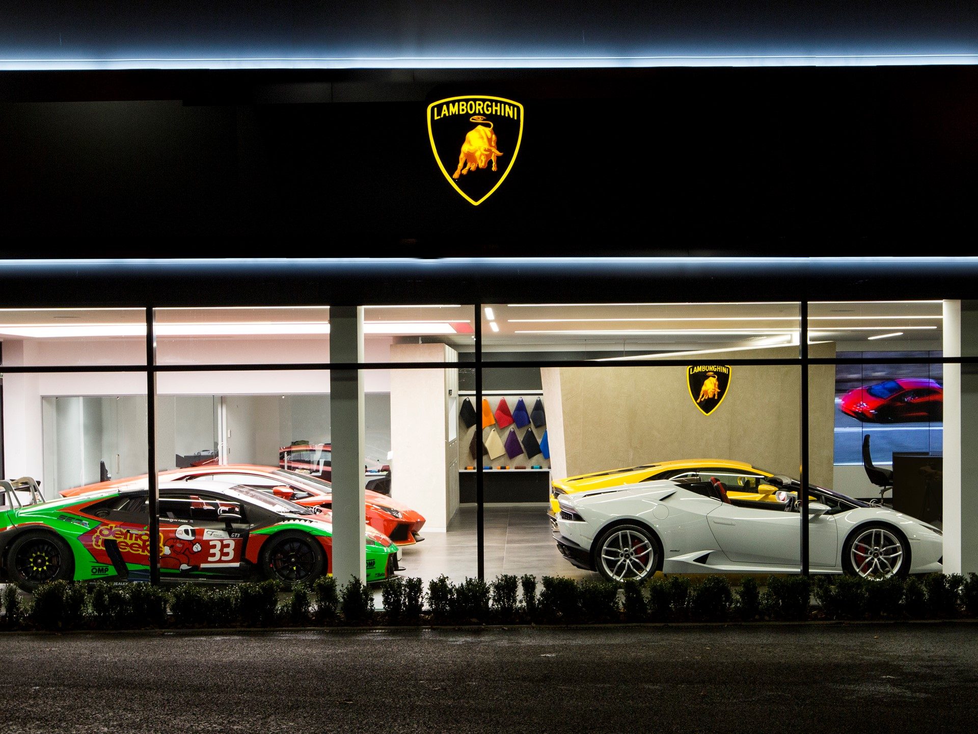 Night exterior of Lamborghini Bristol dealership showing illuminated showroom with Huracan GT3, Aventador, and Huracan models on display