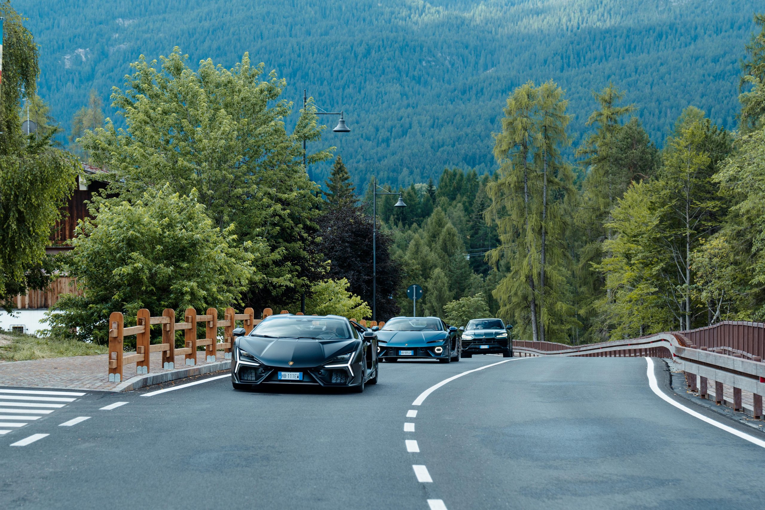 Lamborghini Turns The Mediterranean Into A Showroom With 'Driven By Color' Pop-Ups 13 Convoy of lamborghini vehicles including a black revuelto, light blue huracán tecnica, and dark grey urus driving on a winding mountain road