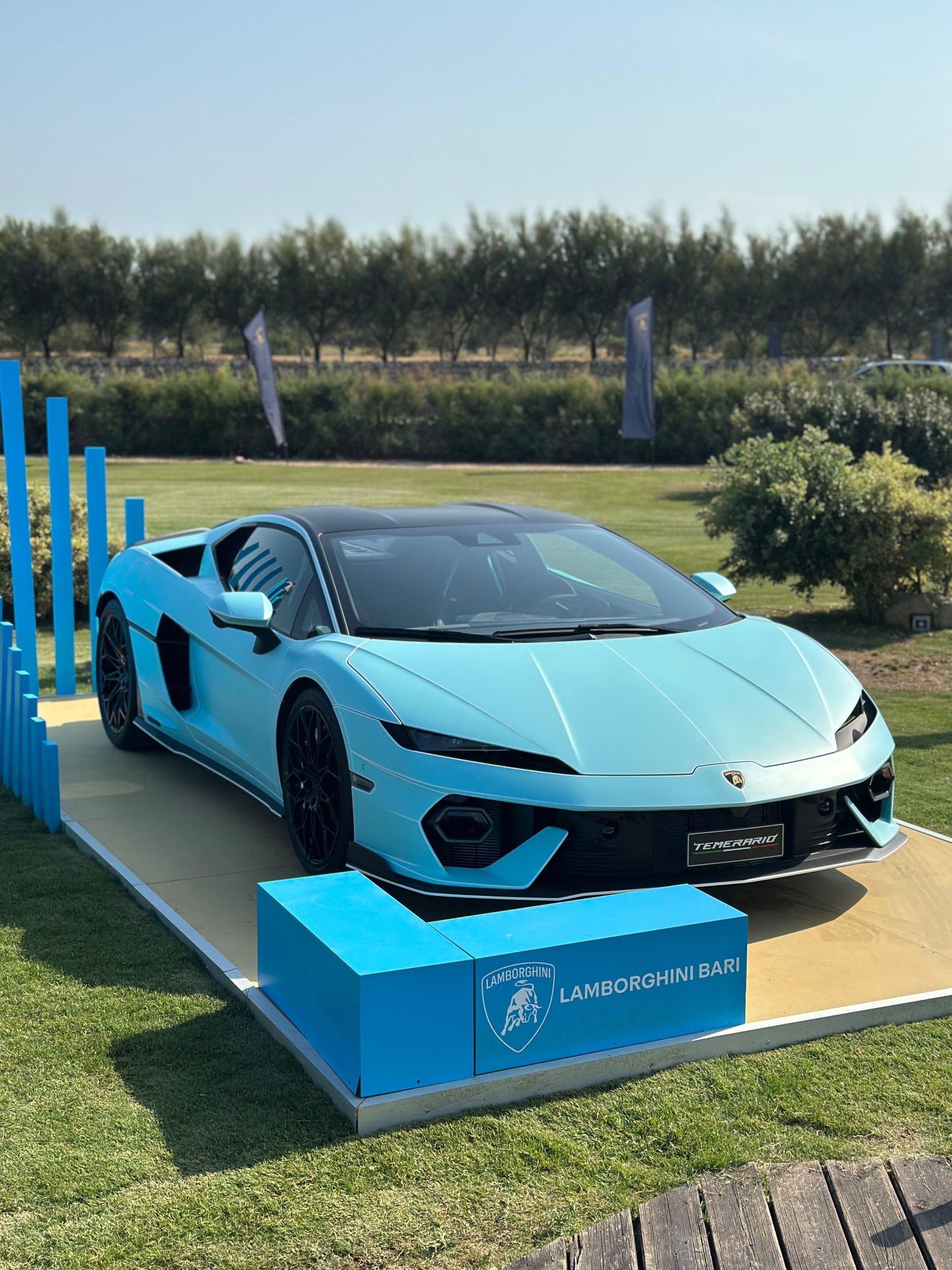 Lamborghini Turns The Mediterranean Into A Showroom With 'Driven By Color' Pop-Ups 7 Light blue lamborghini displayed on a raised platform with a lamborghini bari sign at an outdoor event