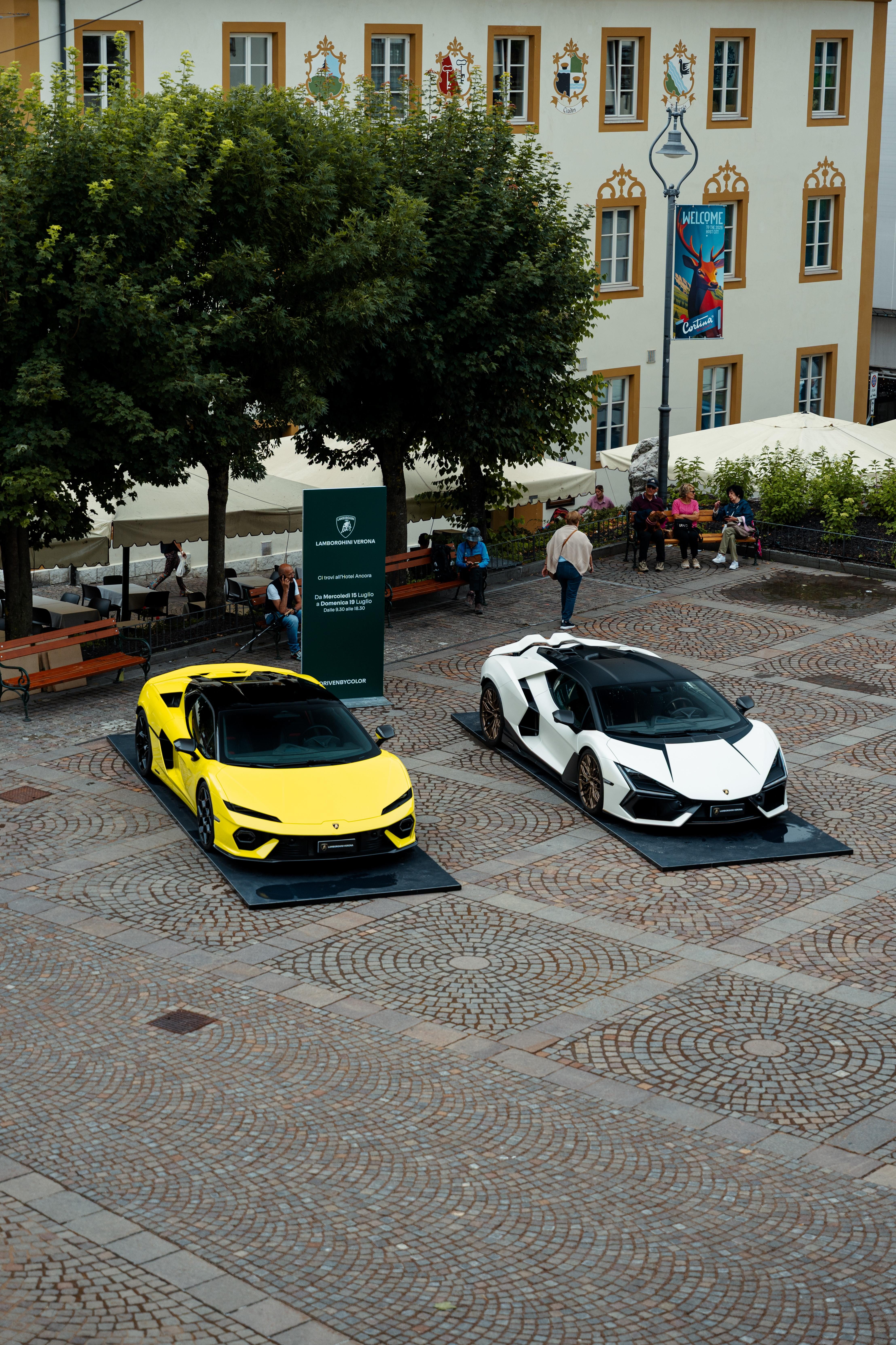 Lamborghini Turns The Mediterranean Into A Showroom With 'Driven By Color' Pop-Ups 11 Two lamborghini revuelto models in yellow and white displayed in a historic town square with onlookers