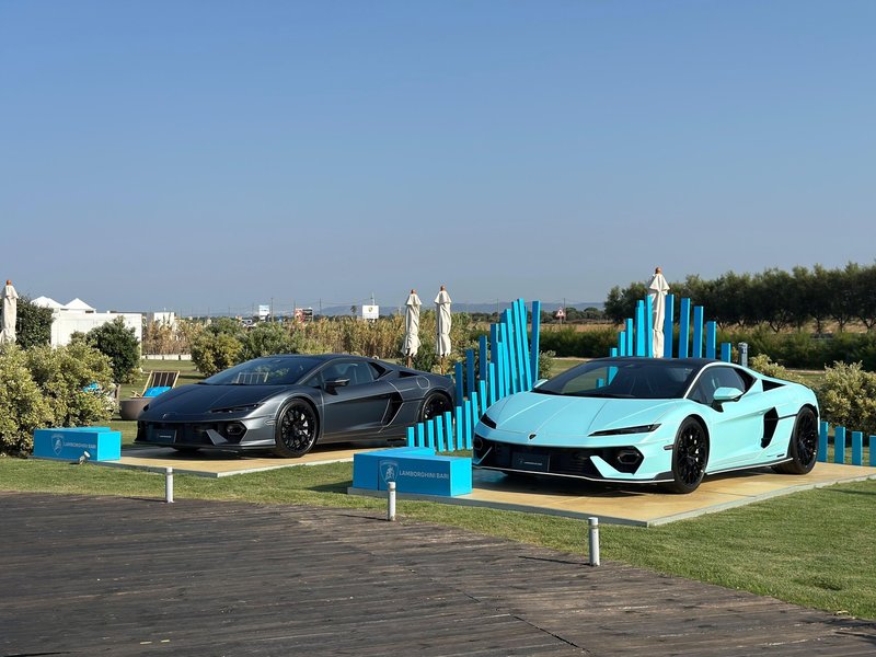 Two Lamborghini Revuelto models in grey and light blue displayed outdoors at a Driven by Color pop-up event with blue decorative elements