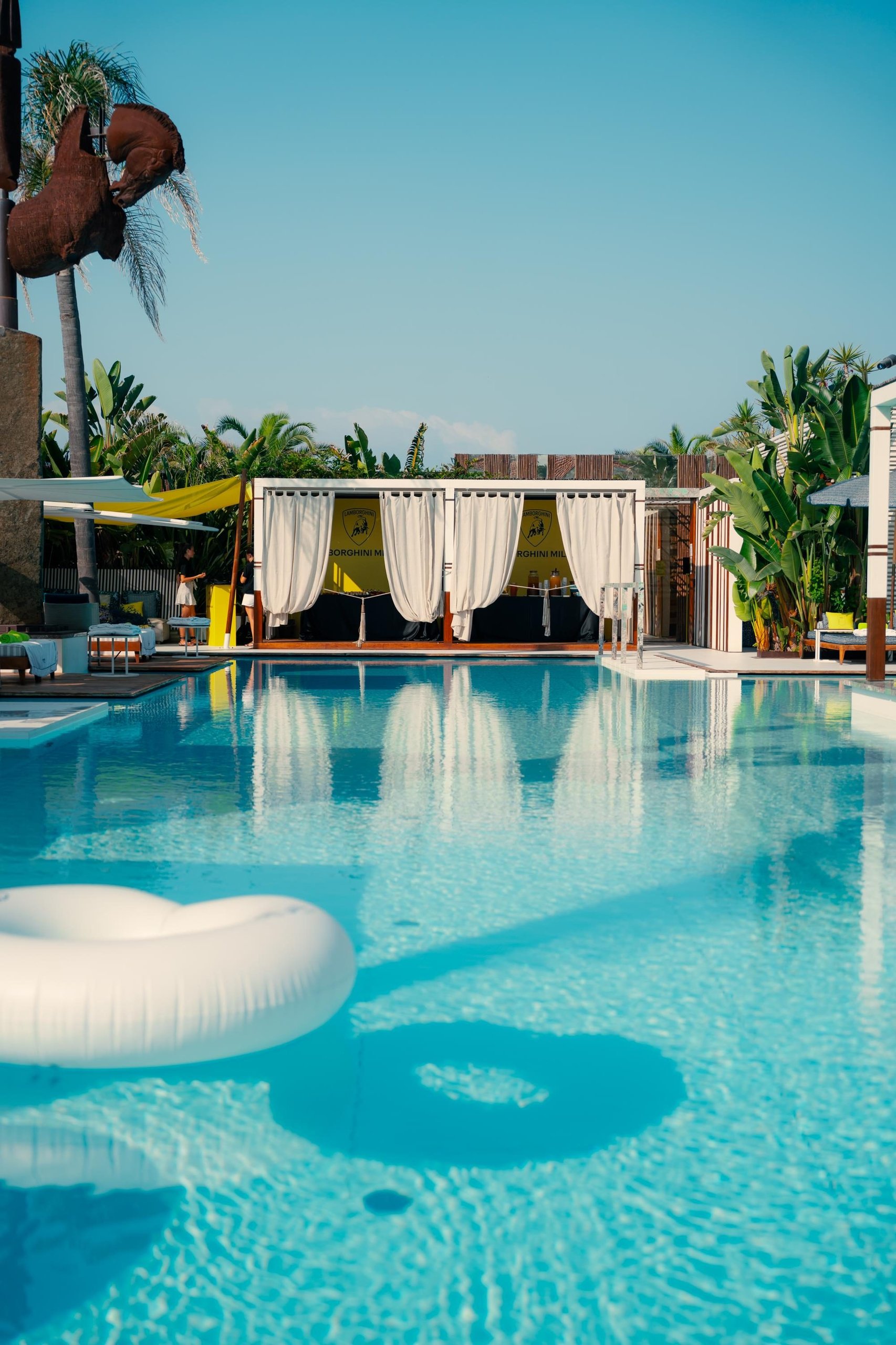 Lamborghini Turns The Mediterranean Into A Showroom With 'Driven By Color' Pop-Ups 3 Luxurious resort pool area with cabanas featuring lamborghini branding under a clear blue sky