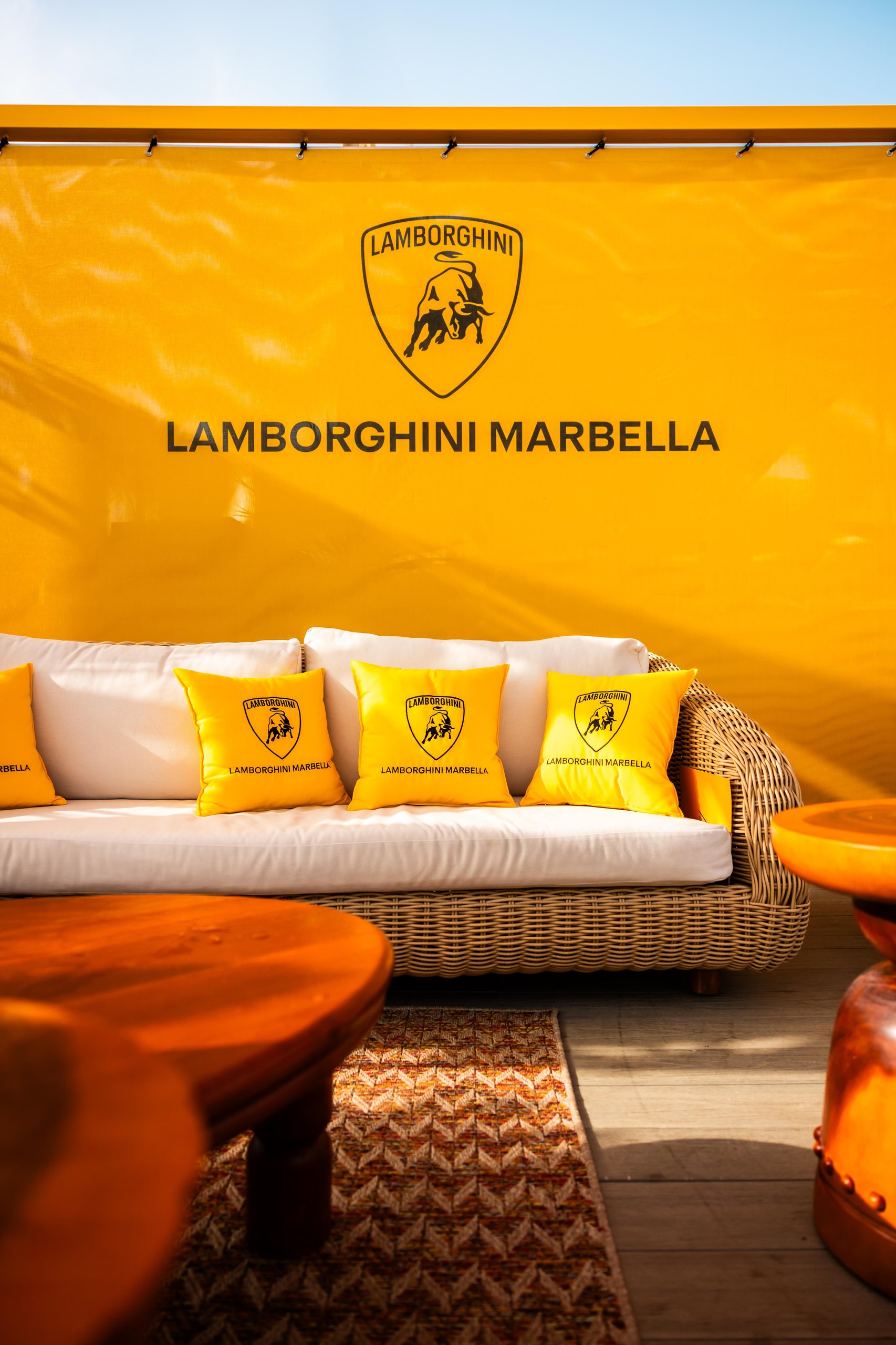Lamborghini Turns The Mediterranean Into A Showroom With 'Driven By Color' Pop-Ups 5 Lounge area with a large yellow banner featuring the lamborghini marbella logo and cushions with the lamborghini emblem