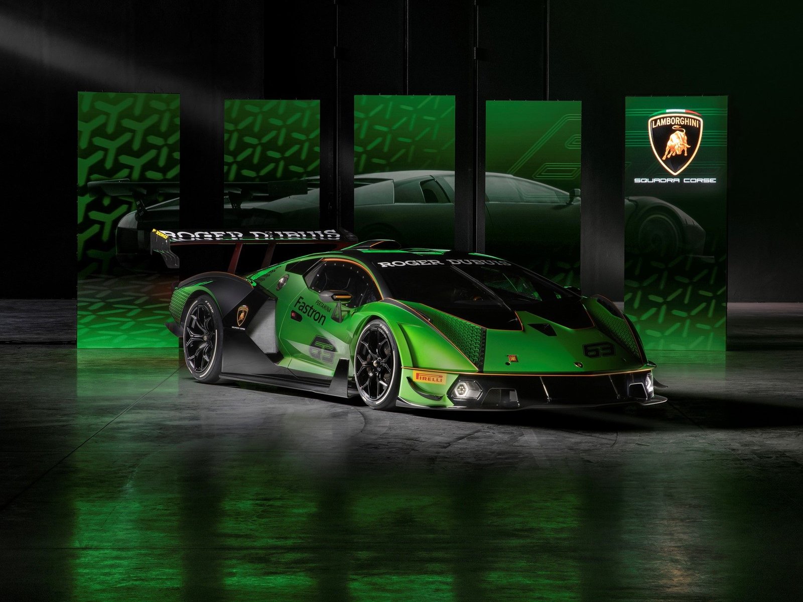 Lamborghini Essenza SCV12 showing aggressive aero bodywork, large rear wing, hexagonal livery patterns, and racing number 63 in a studio with heritage model display panels