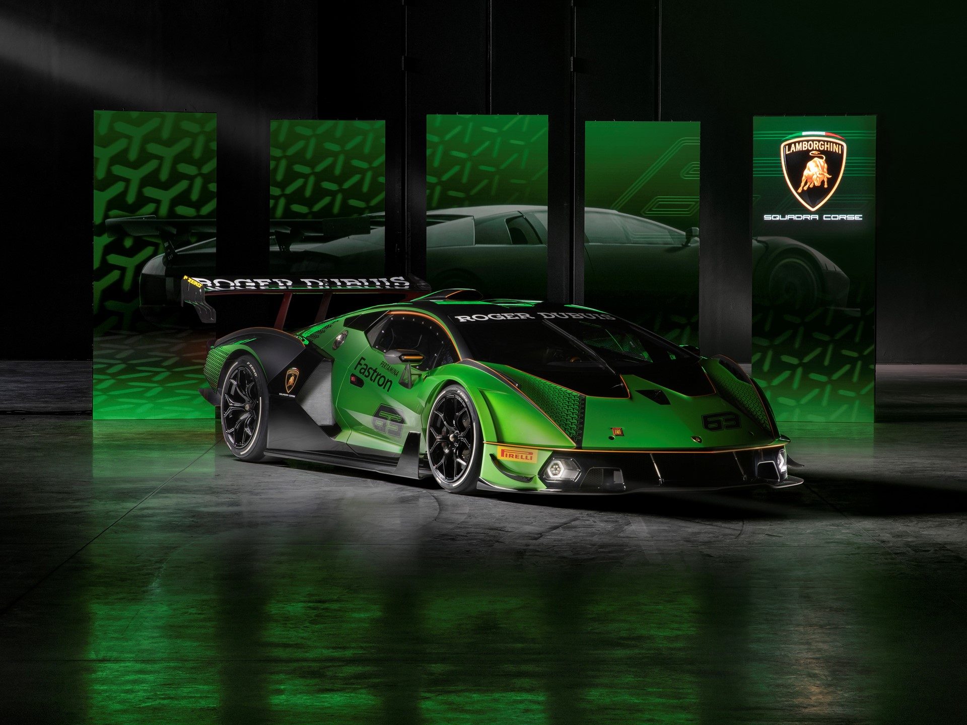 Lamborghini essenza scv12 showing aggressive aero bodywork, large rear wing, hexagonal livery patterns, and racing number 63 in a studio with heritage model display panels