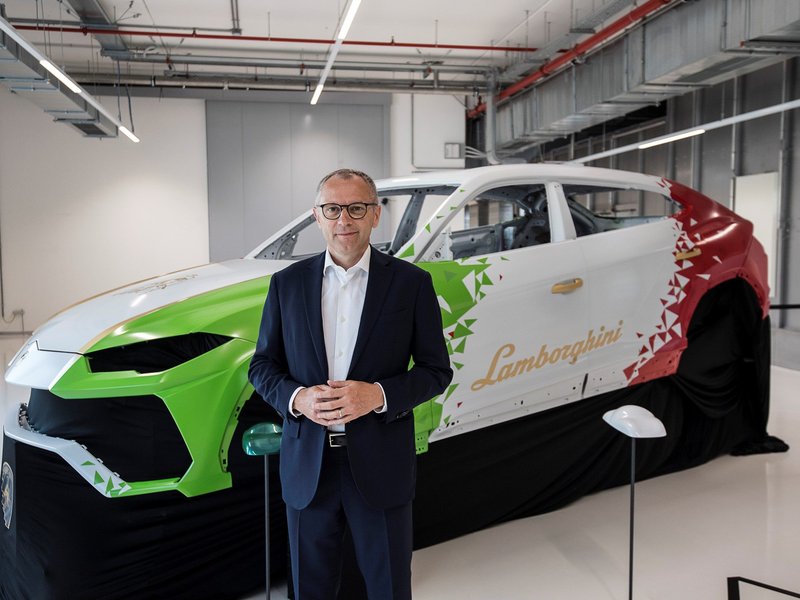 A Lamborghini executive stands beside a partially assembled Urus body shell painted in Italian tricolor livery inside the Sant'Agata Bolognese factory