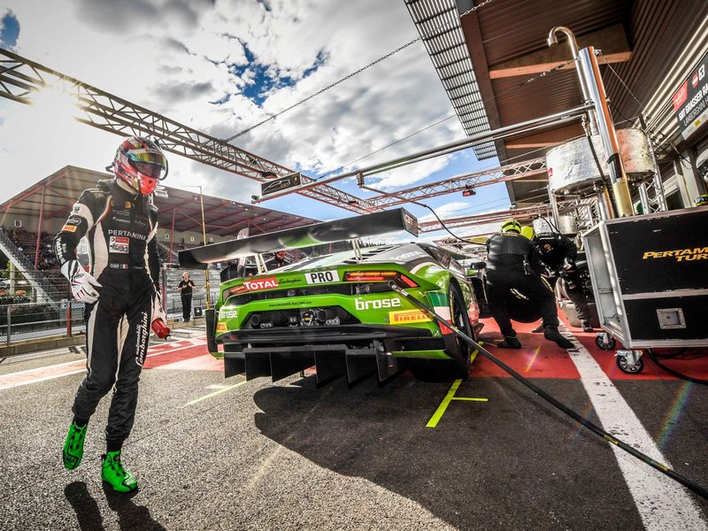 Lamborghini Huracán GT3 in green livery being serviced in the pit lane with a driver walking away in full racing gear