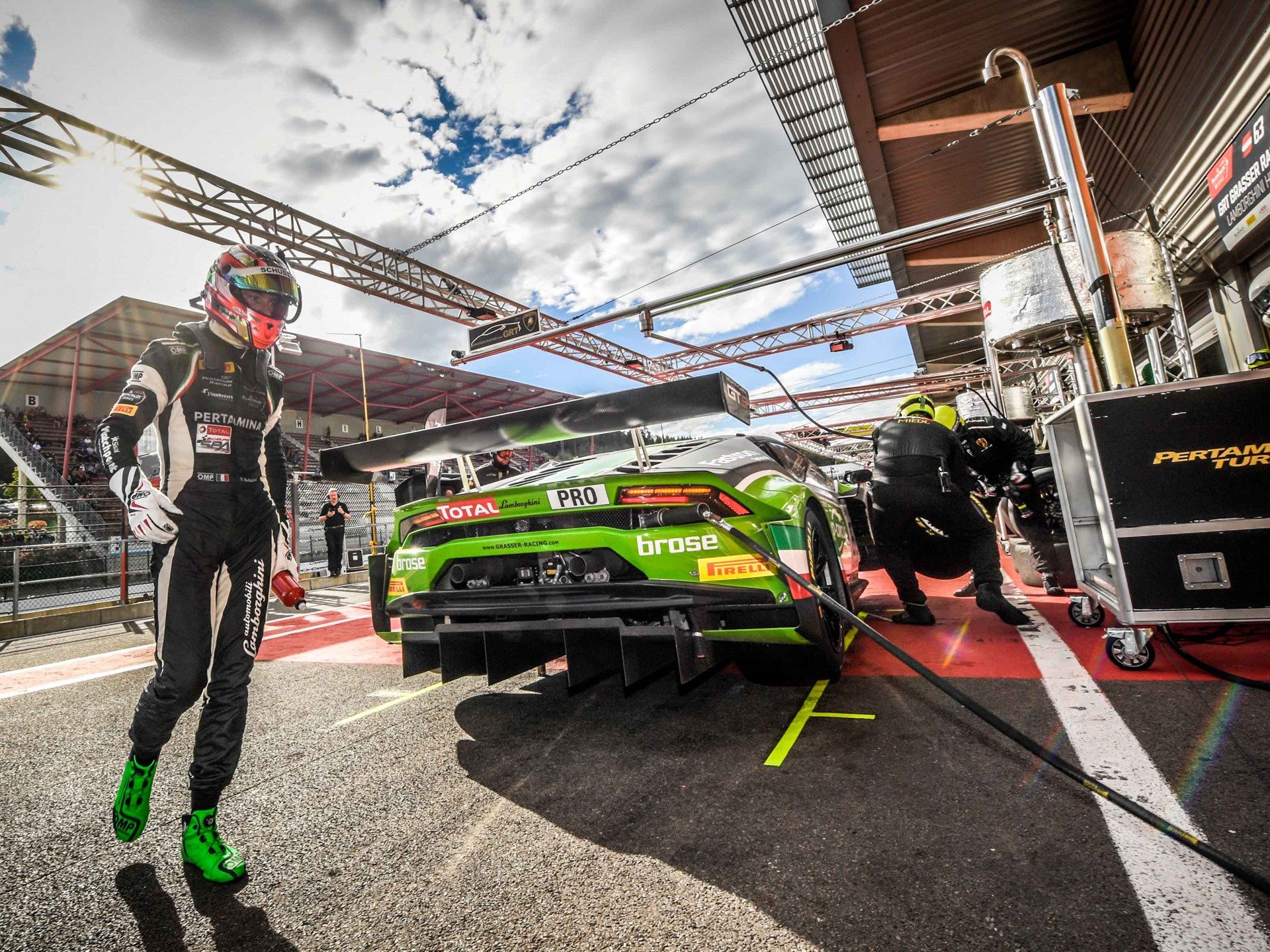 Lamborghini Huracán GT3 in green livery being serviced in the pit lane with a driver walking away in full racing gear