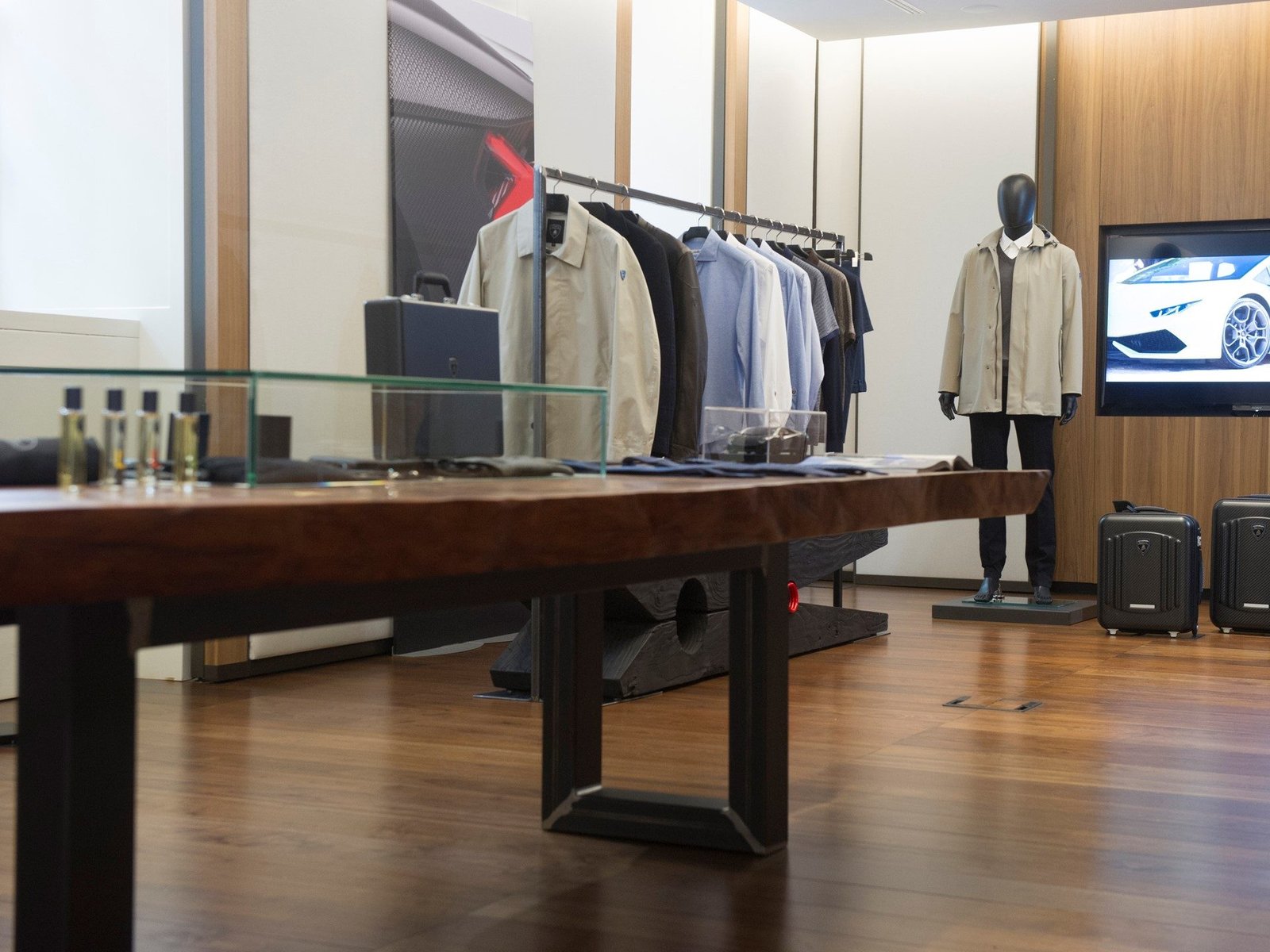Lamborghini lifestyle boutique displaying Fall Winter 2017/18 fashion collection with garments, a mannequin in a beige jacket, and a Huracán on screen