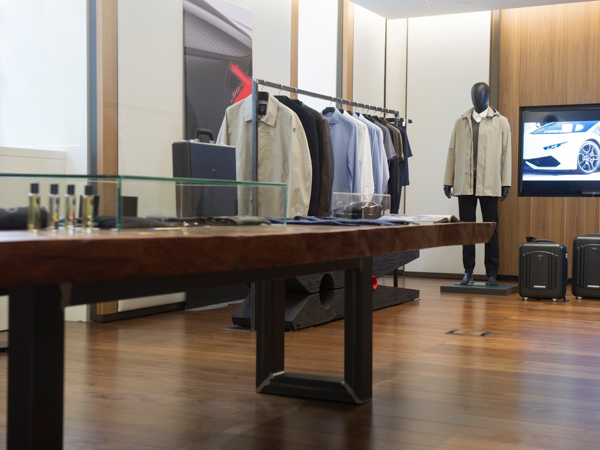 Lamborghini lifestyle boutique displaying Fall Winter 2017/18 fashion collection with garments, a mannequin in a beige jacket, and a Huracán on screen