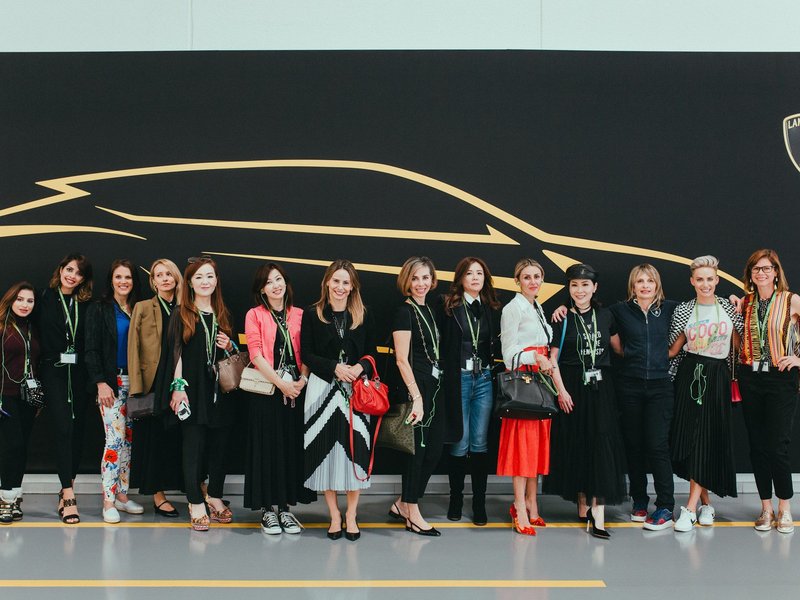 Women attending a Lamborghini FAB event, standing before a backdrop with the Lamborghini logo and a gold car silhouette