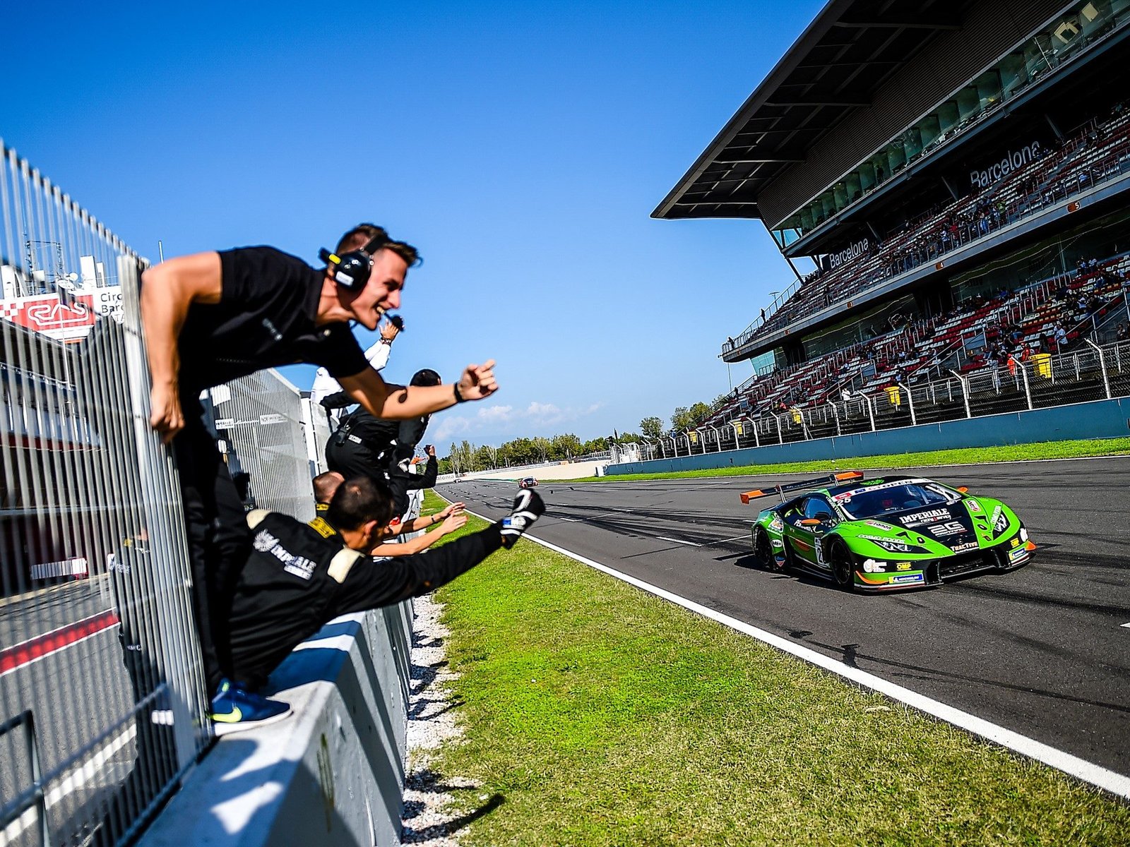 Green Lamborghini Huracán GT3 racing past its pit crew at the Barcelona circuit during the 2018 International GT Open finale