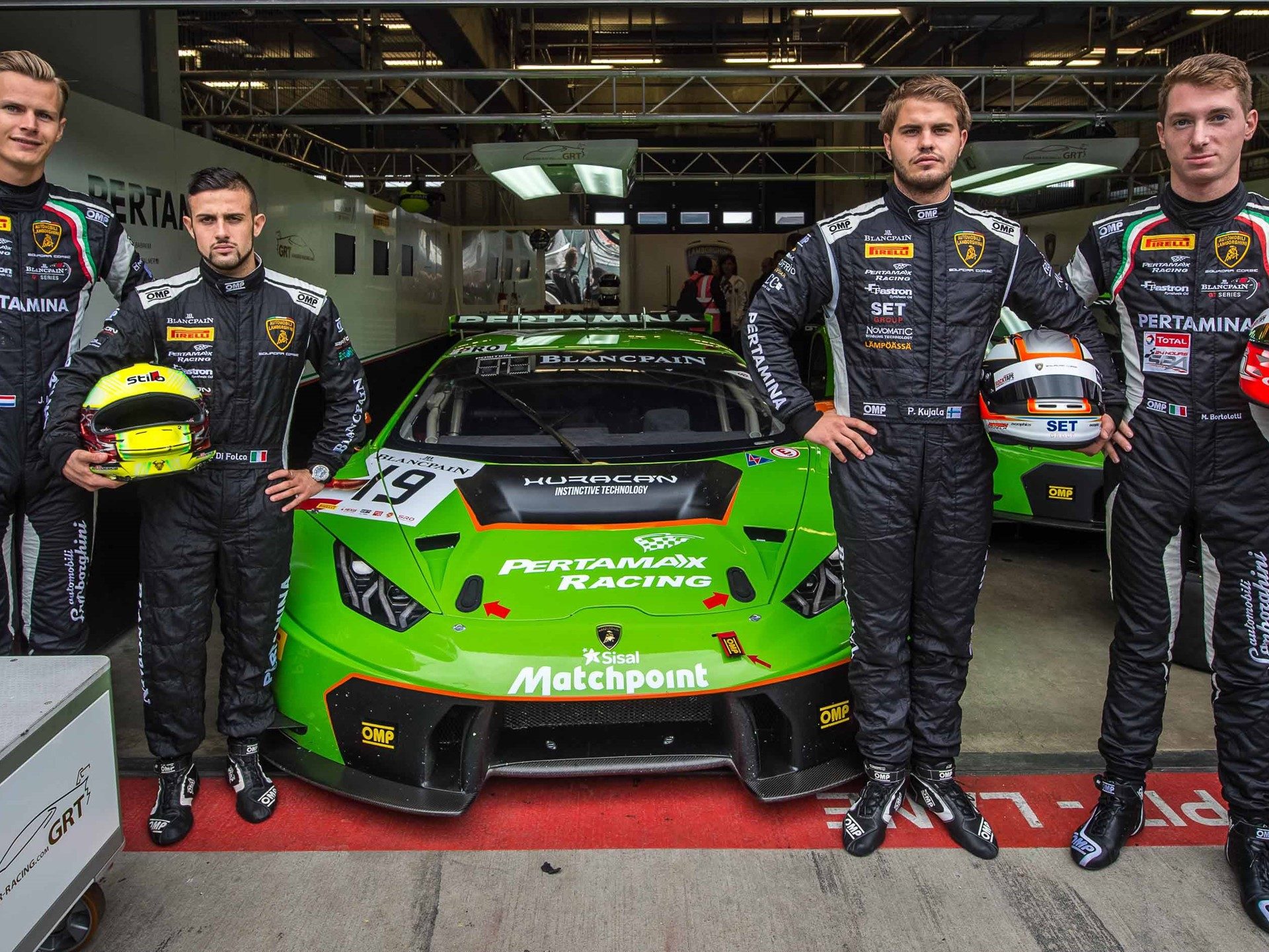 Four Grasser Racing Team drivers in black racing suits pose alongside a bright green Lamborghini Huracan GT3 in the pit garage