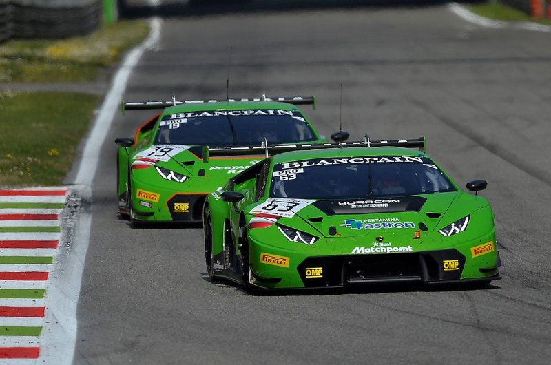 Two green Lamborghini Huracán GT3 race cars battling for position on a racetrack, showcasing aerodynamic bodywork and large rear wings