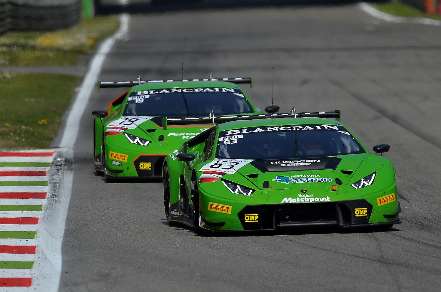 Two green lamborghini huracán gt3 race cars battling for position on a racetrack, showcasing aerodynamic bodywork and large rear wings