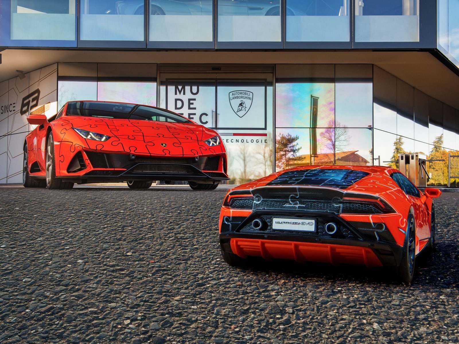 Orange Lamborghini Huracán EVO with puzzle-piece livery parked beside a standard Huracán EVO at a Lamborghini dealership