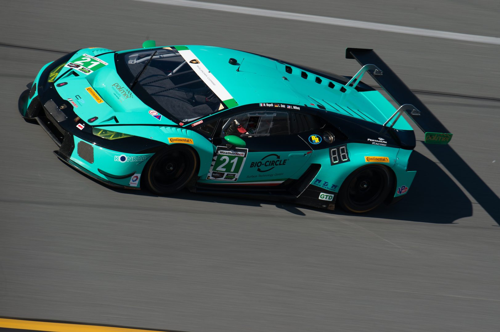 Teal green Lamborghini Huracán GT3 number 21 racing on track at Daytona, captured from an elevated perspective showing the large rear wing and vented engine cover