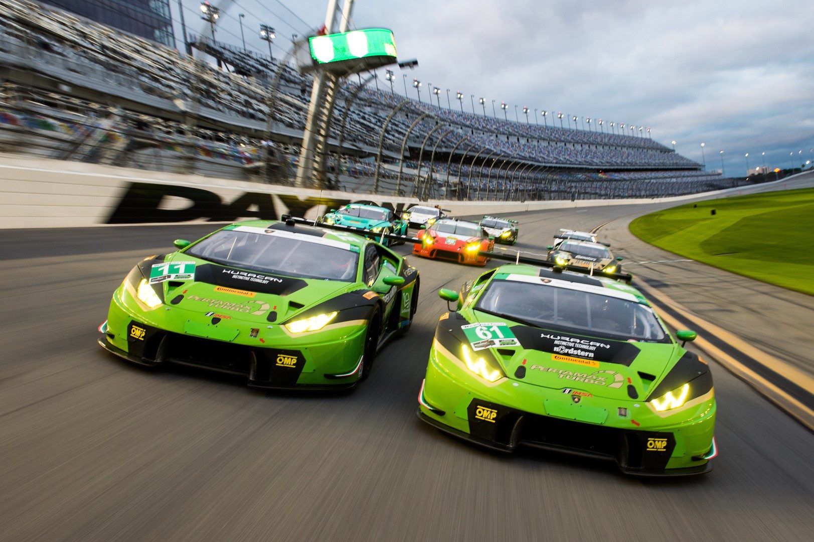 Two green Lamborghini Huracán GT3 race cars leading a pack of competitors on the Daytona International Speedway banking