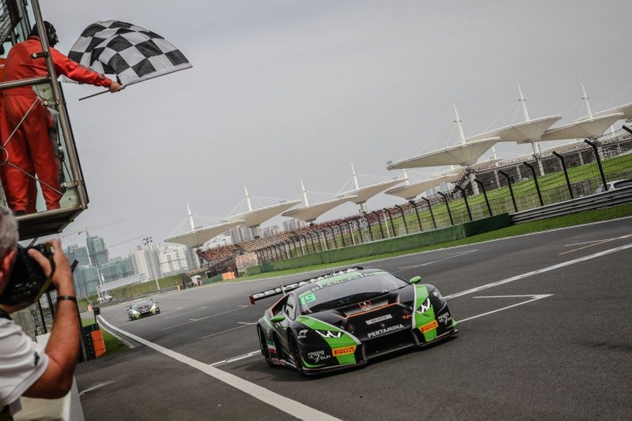Black and green Lamborghini Huracán GT3 crosses the finish line under a checkered flag during a GT championship race