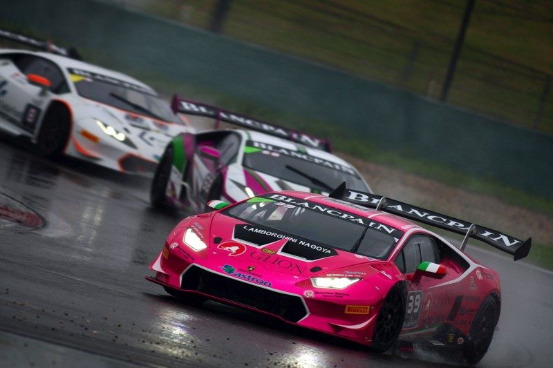 Lamborghini Huracán GT3 race cars navigate heavy spray on a wet Shanghai International Circuit, with a prominent pink-liveried car among the competitors
